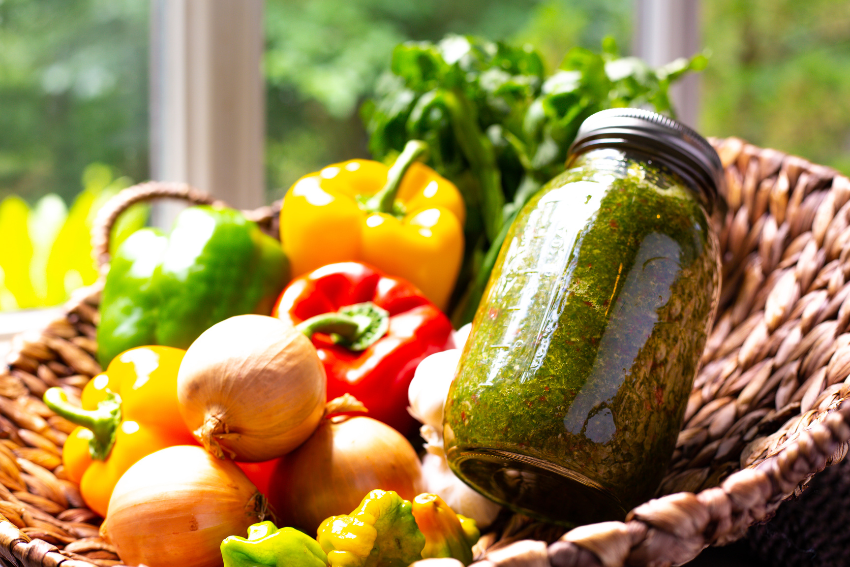 Homemade sofrito in a jar surrounded by fresh vegetable ingredients in a basket